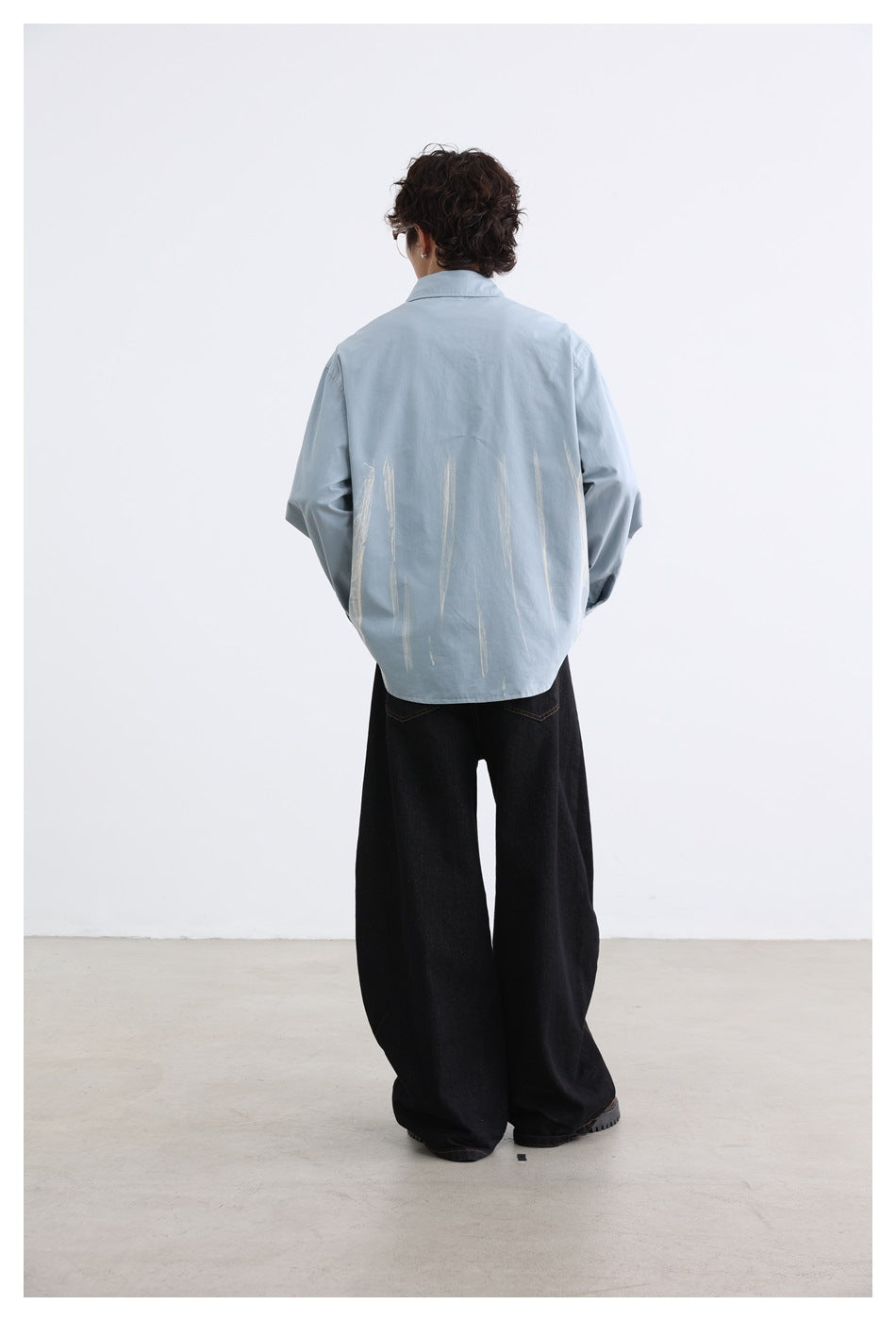 Rear view of a model wearing a pale blue button-up shirt with light brushstroke graphics.