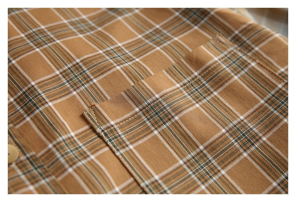 Close-up of camel plaid shirt fabric with a stitched pocket edge and a partial tan button.