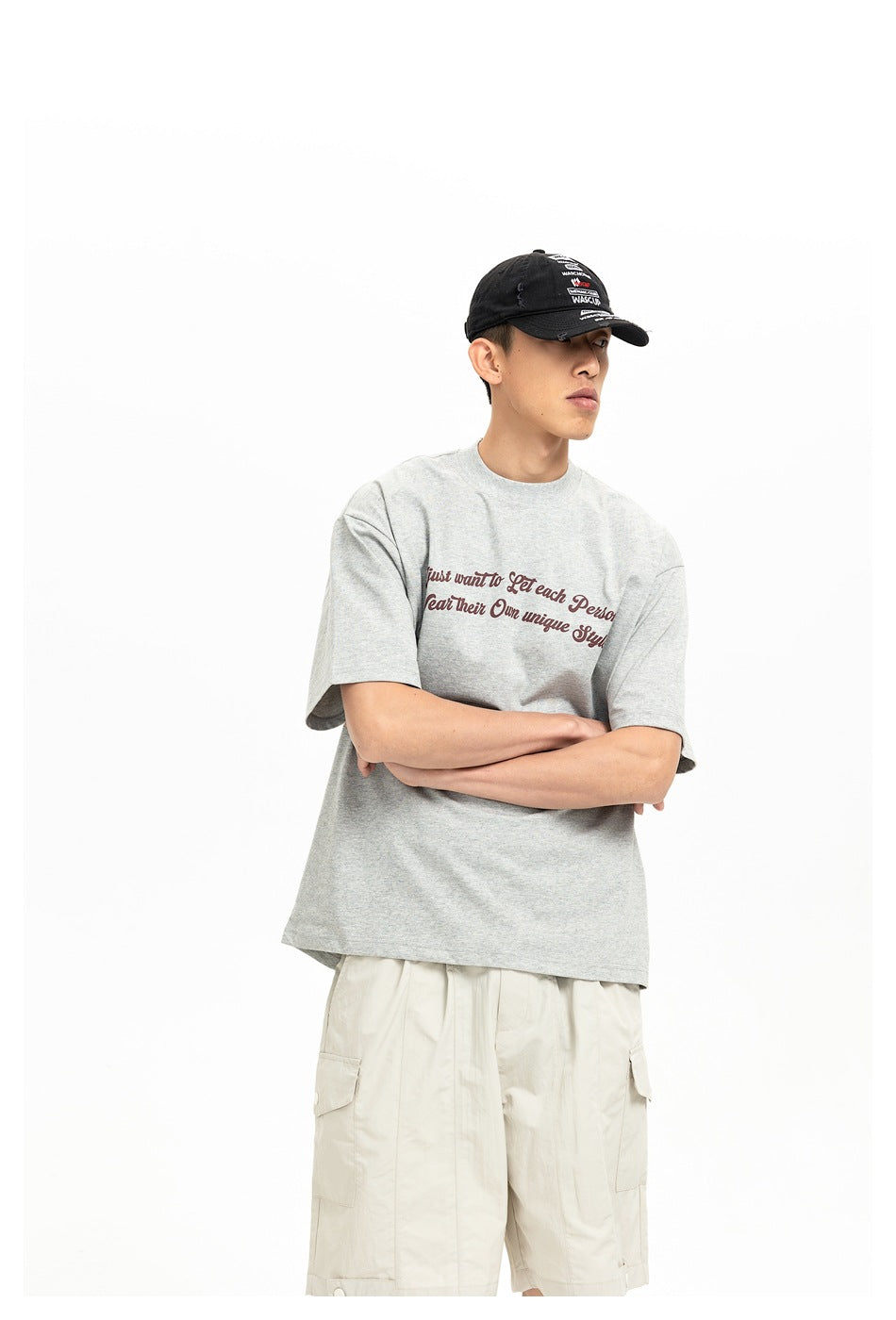 Model wearing a light gray graphic T-shirt and cream cargo shorts, arms crossed; the shirt print is partly obscured.