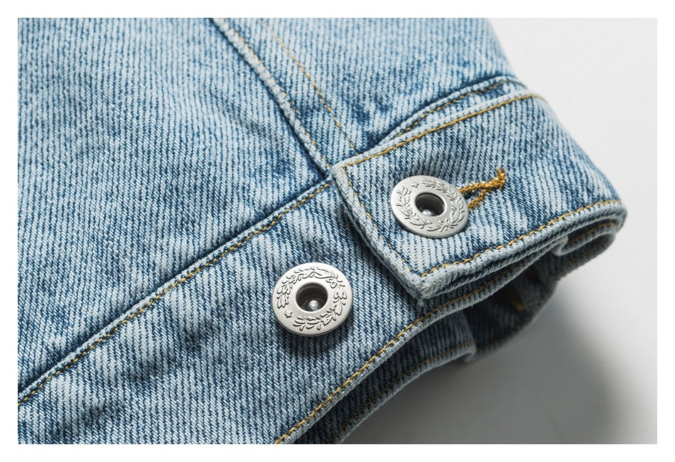 Close-up of two decorative metal buttons and contrast stitching on a light blue denim jacket.