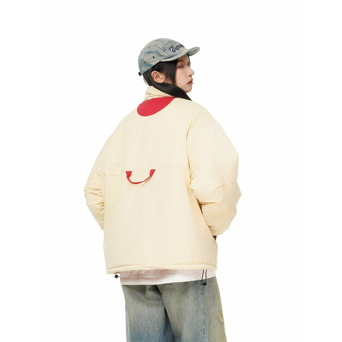 Rear three-quarter view of a model in a cream padded jacket with red back accents and wide jeans.