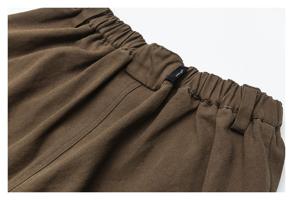 Close-up of brown trousers showing an elasticated waistband, belt loops, and a small black label.