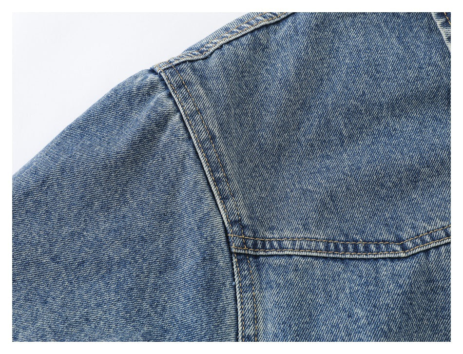 Close-up of the blue washed denim jacket's shoulder seam and back yoke stitching.