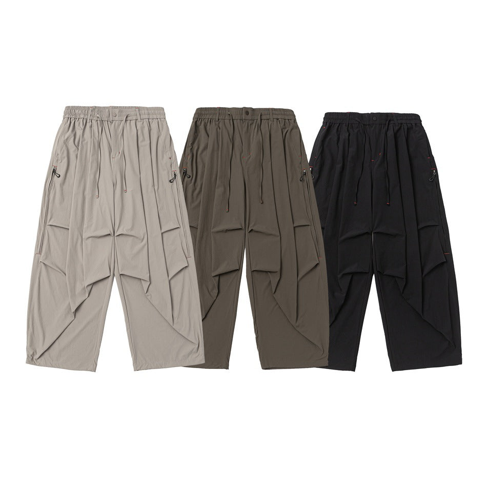 Front view of wide-leg trousers in light gray, olive gray, and black, with elastic waists, drawstrings, and large pockets.