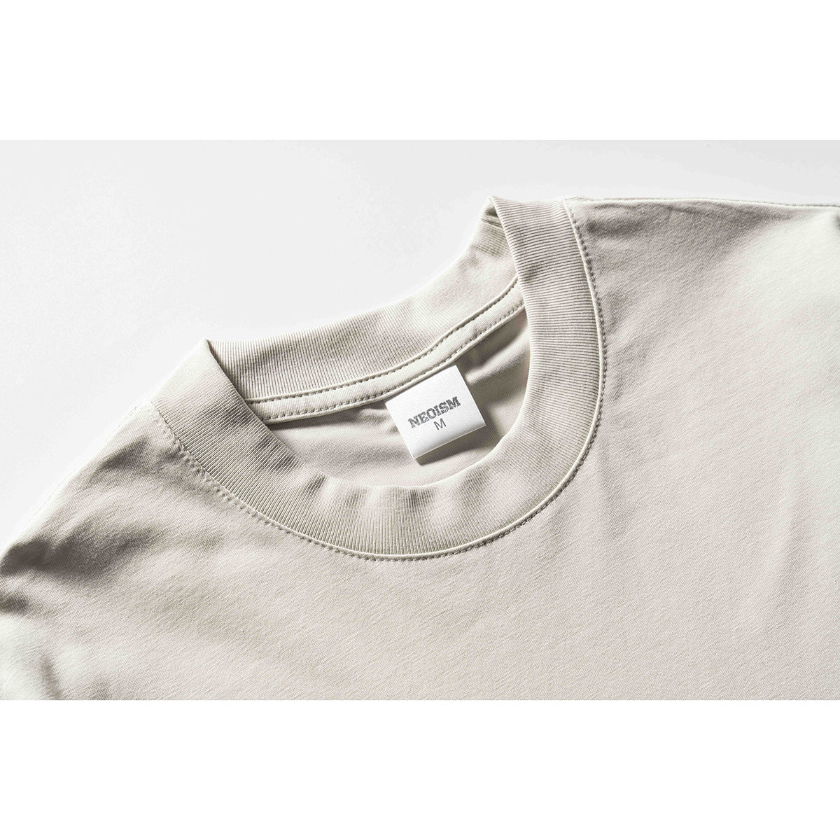 Close-up of a light beige T-shirt's ribbed crew neck and inner size label.