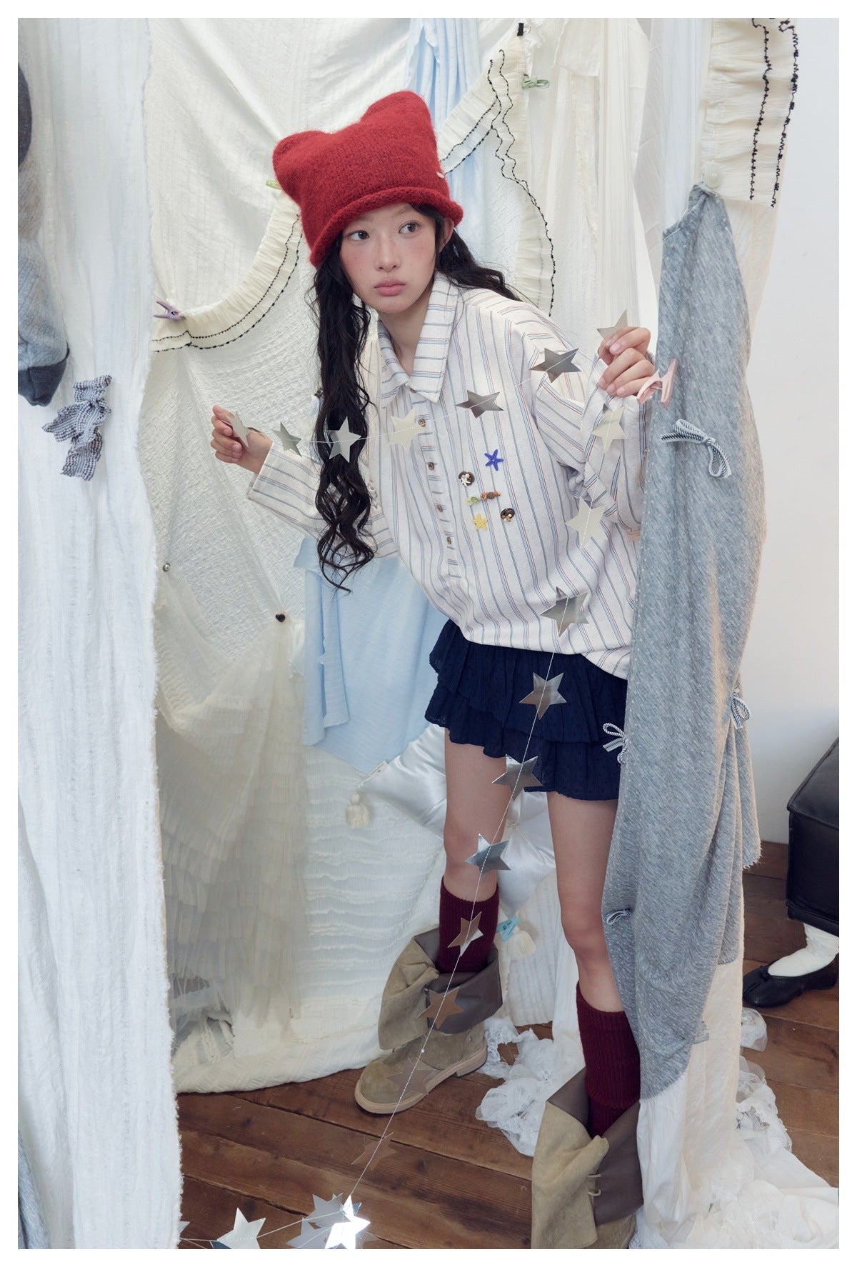 Model in the striped half-button shirt with chest button charms, navy ruffled skirt, red hat and burgundy socks