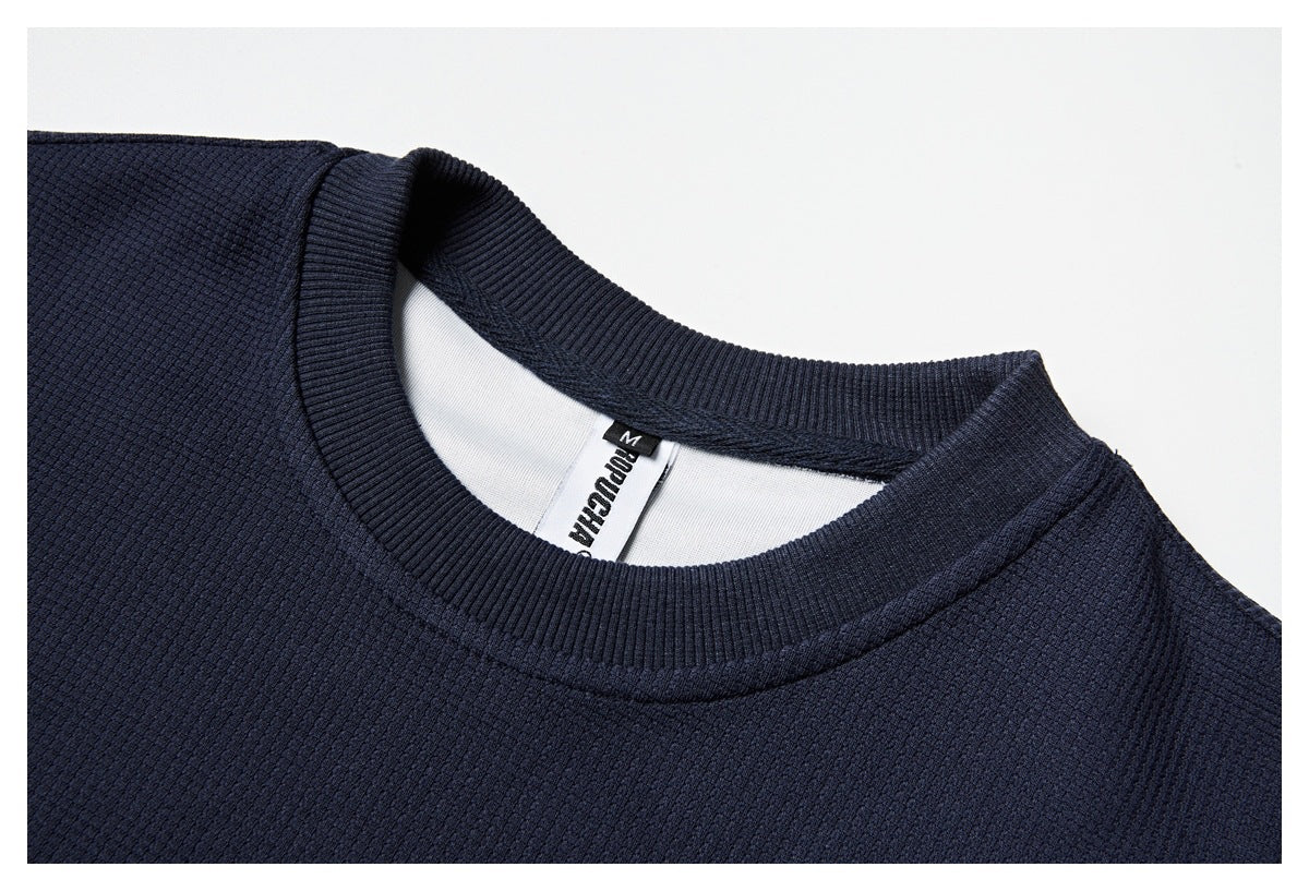 Close-up of the navy sweatshirt's ribbed crew neckline, textured fabric, and inside neck label.