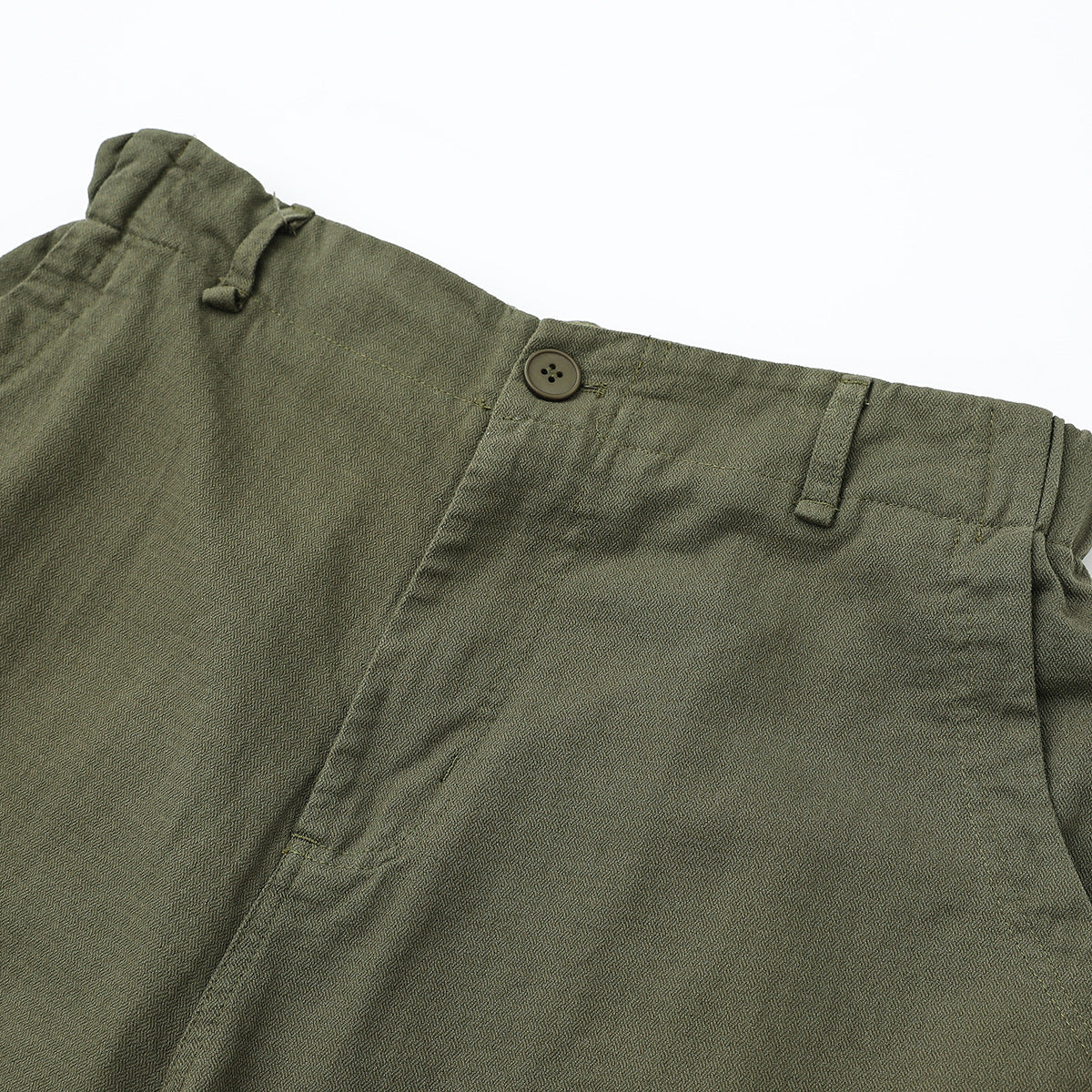 Close-up of olive-gray cargo pants showing the buttoned waistband, belt loops, and front pocket seam.