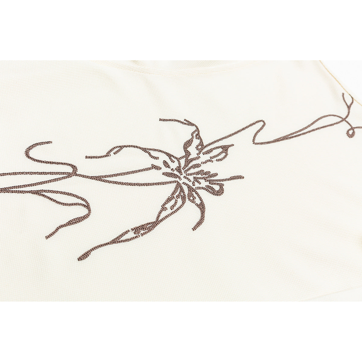 Close-up of dark brown embroidered floral line art on ivory shirt fabric.