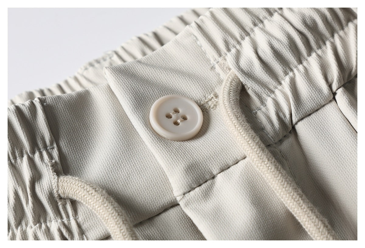 Close-up of light beige pants showing a gathered elastic waistband, button closure, and braided drawstring.