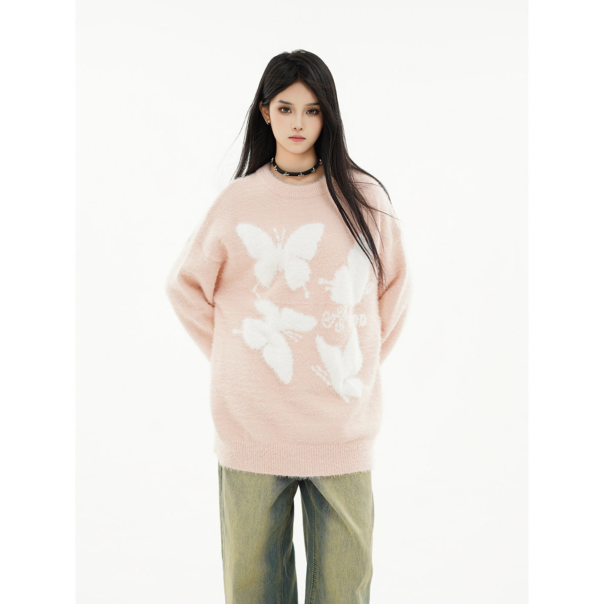 Model wearing an oversized pale pink sweater with white butterfly motifs and loose green-gray jeans.