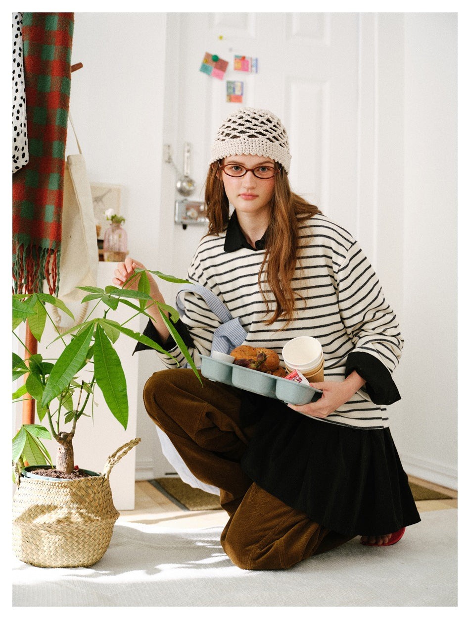 Seated model wearing a cream-and-black striped long-sleeve top with a black collar and cuffs.