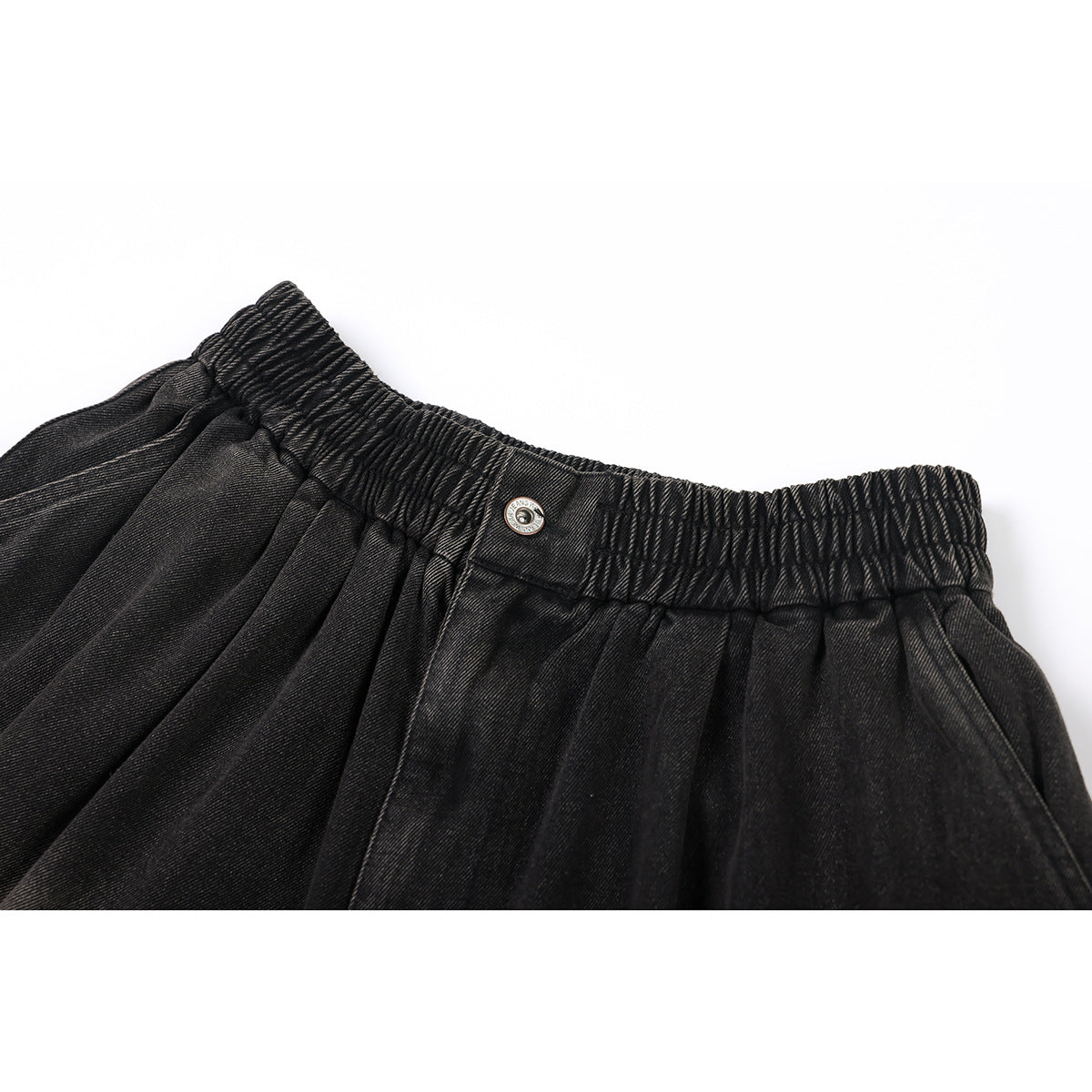 Close-up of black denim trousers showing a gathered elastic waistband, metal button, and pleated fabric.