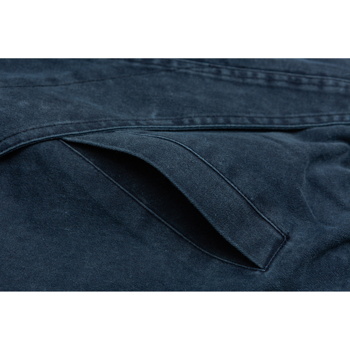 Close-up of a slanted welt pocket and stitched seams on dark blue denim.