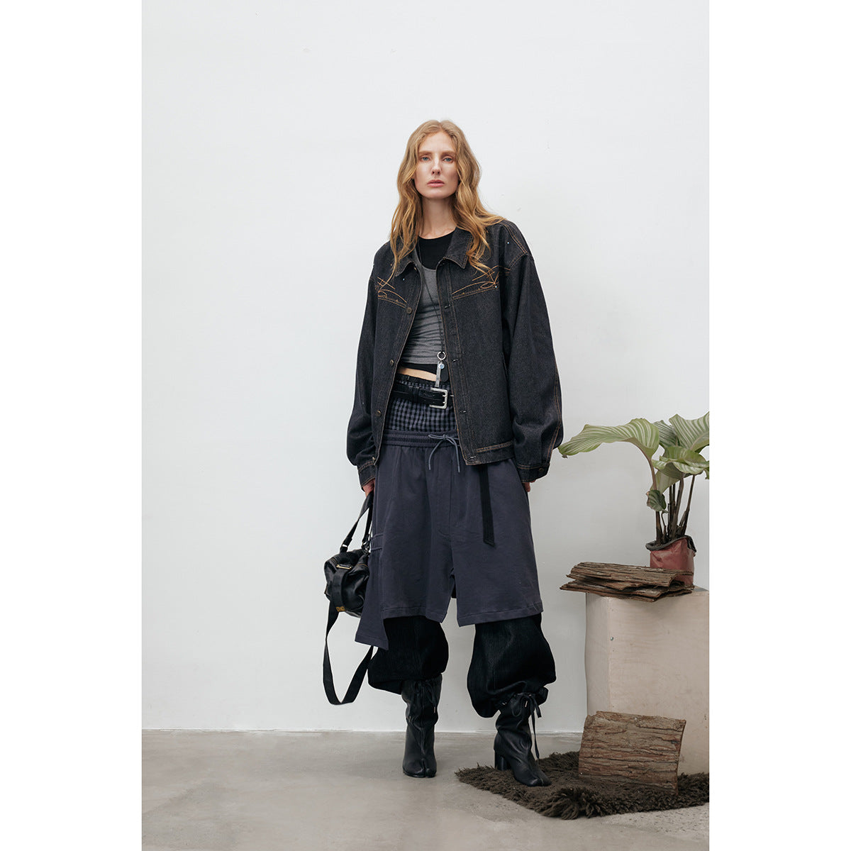 Model wearing an oversized black denim jacket with tan stitched decoration, layered over dark clothing.