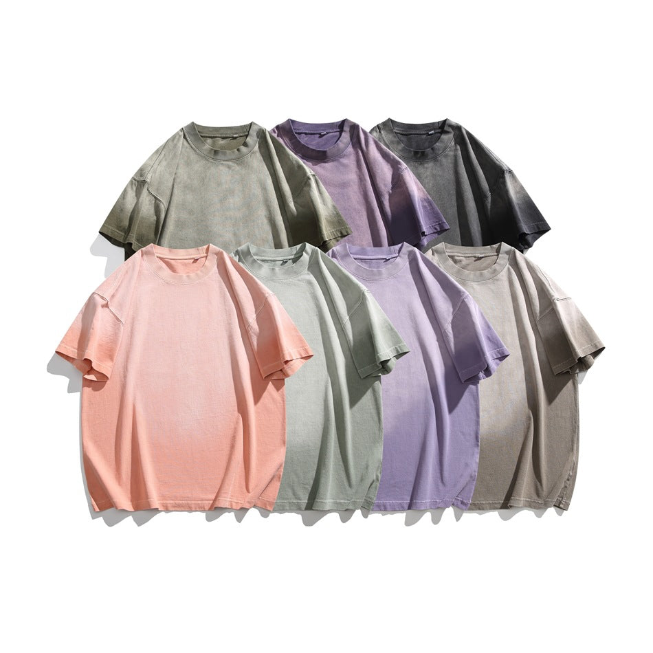 Seven plain oversized short-sleeve T-shirts arranged together in muted green, purple, charcoal, pink, sage, lavender, and