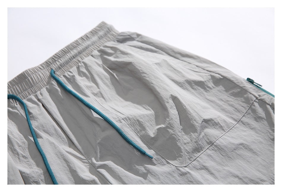 Close-up of light gray shorts with a gathered waistband, teal drawstrings, and front pockets.