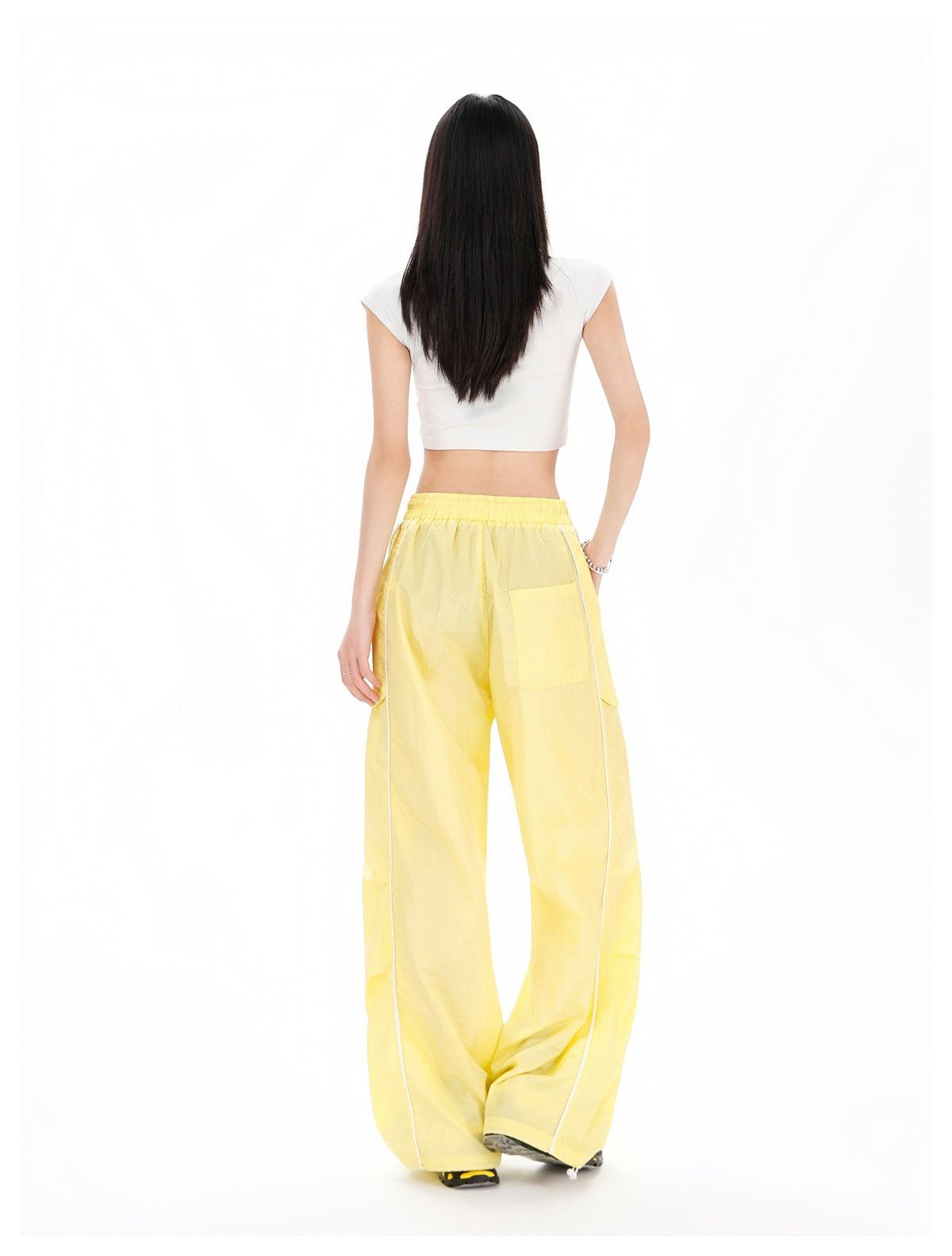 Rear view of a model wearing pale yellow wide-leg pants with an elastic waist and white piping, paired with a white cropped