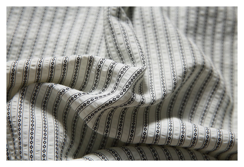 Close-up showing the cream shirt's black geometric stripe pattern and draped fabric.