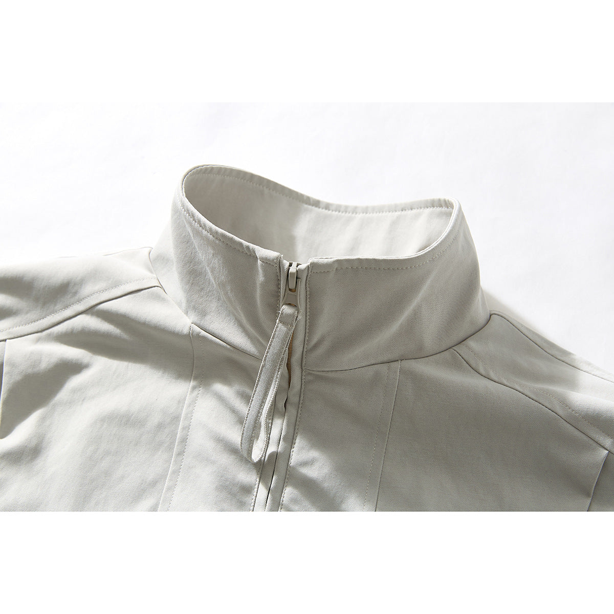 Close-up of an off-white jacket's stand collar, front zipper, and shoulder seams.