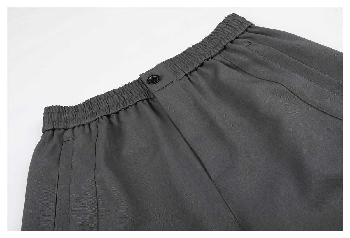 Close-up of charcoal shorts showing the gathered elastic waistband, button closure, and front seam.