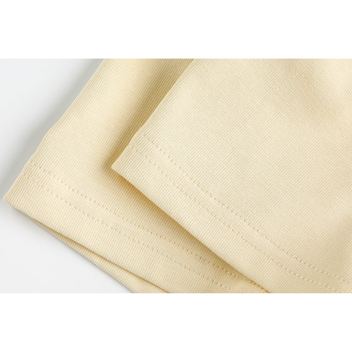 Close-up of pale yellow T-shirt fabric showing the double-stitched sleeve or hem edge.