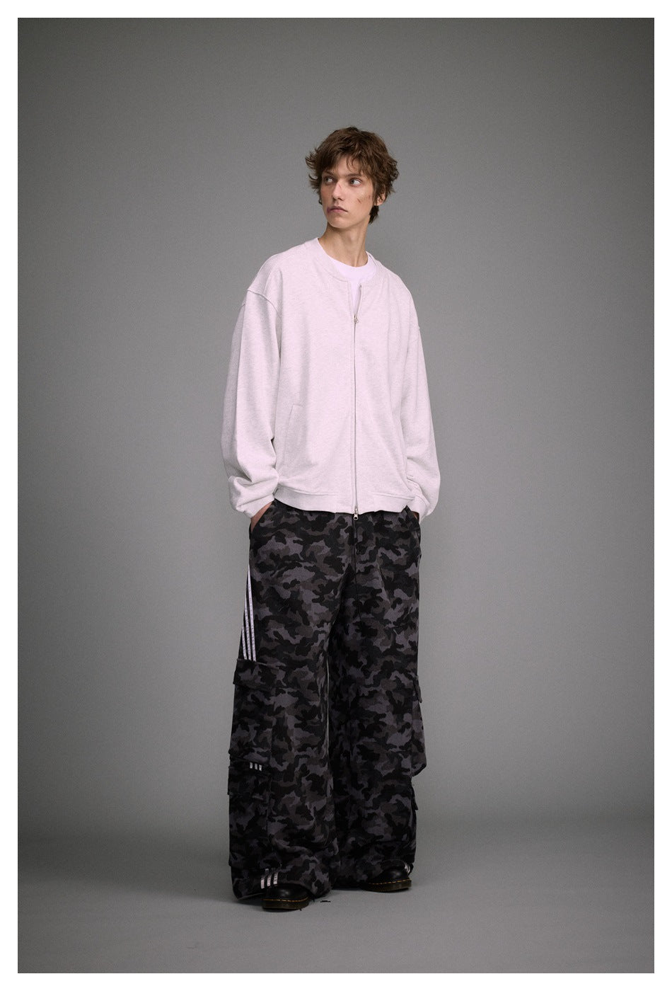 Full-length model wearing a pale pink zip-front jacket and loose black-and-gray camouflage cargo pants.
