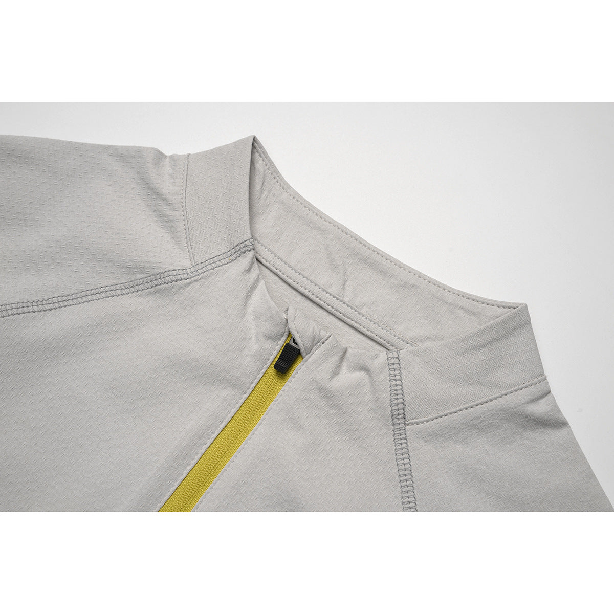 Close-up of a light gray quarter-zip top's stand collar, yellow zipper, and stitched seams.