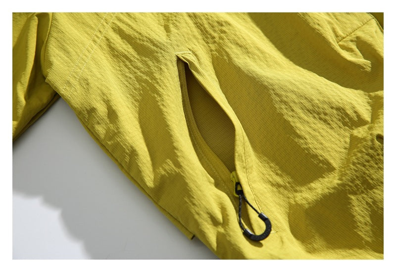 Close-up of a yellow jacket pocket opening with a black corded hook attached near the edge.