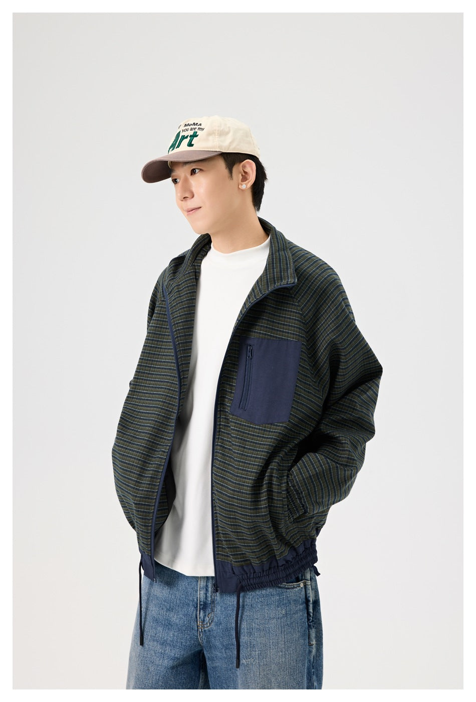 Man wearing a dark green and navy striped jacket with a navy zip chest pocket, white shirt, jeans, and cream cap.
