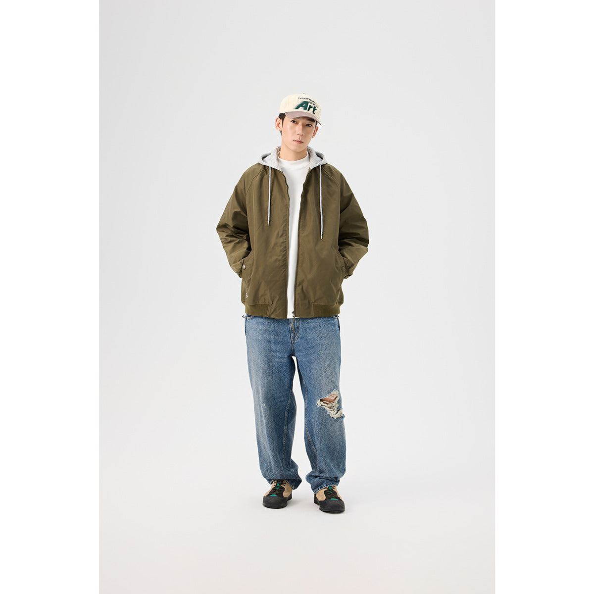 Front view of a model wearing an olive jacket with a gray drawstring hood, white shirt, and loose blue jeans.
