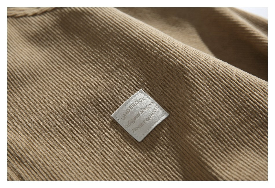 Close-up of tan ribbed corduroy fabric with a small square sewn label bearing English lettering.
