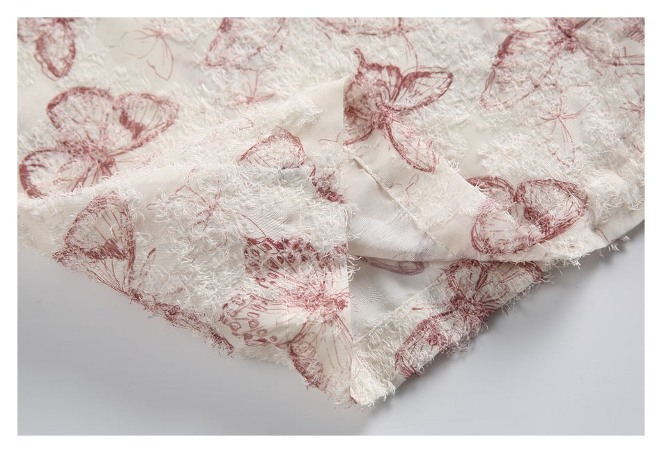 Close-up of a folded garment edge in ivory fabric with raised white texture and dusty rose butterflies.