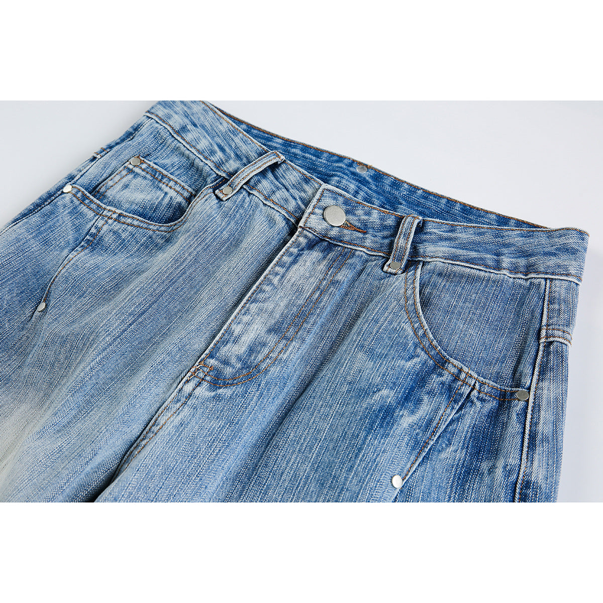 Close-up of the front waist and pockets of light blue faded jeans with metal rivets and a button.