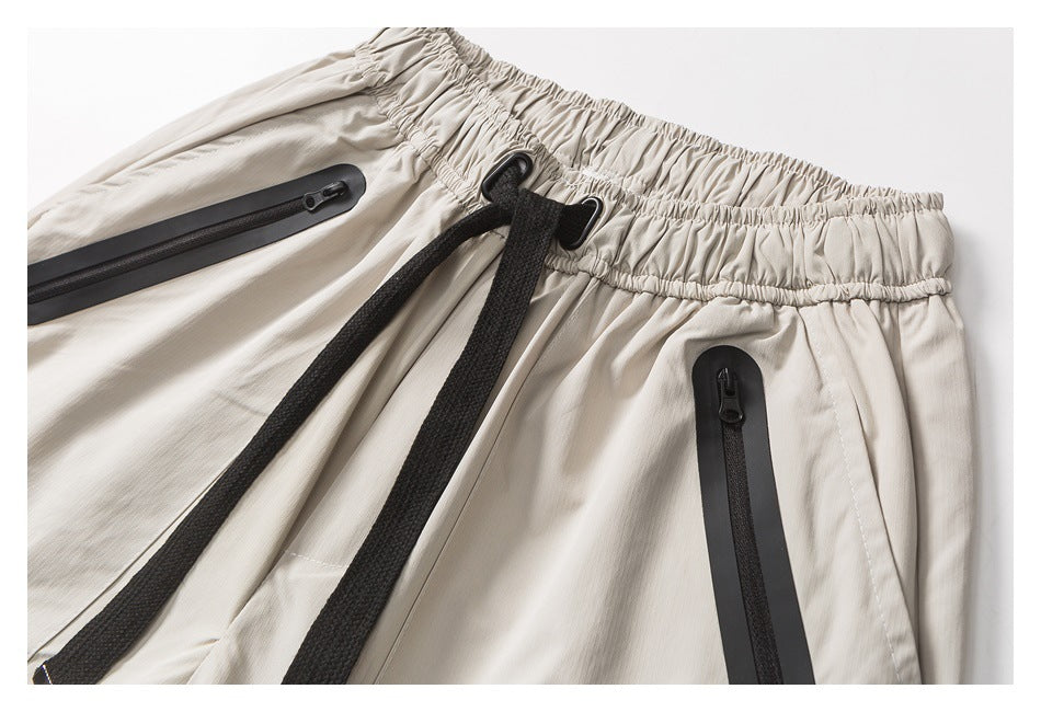 Close-up of light beige shorts with a gathered waistband, black drawcord, and black-trimmed zip pockets.
