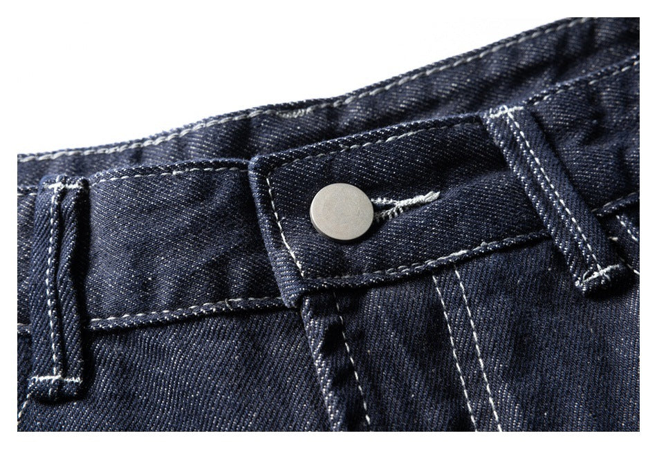 Extreme close-up of the jeans' silver waistband button and contrast stitching.
