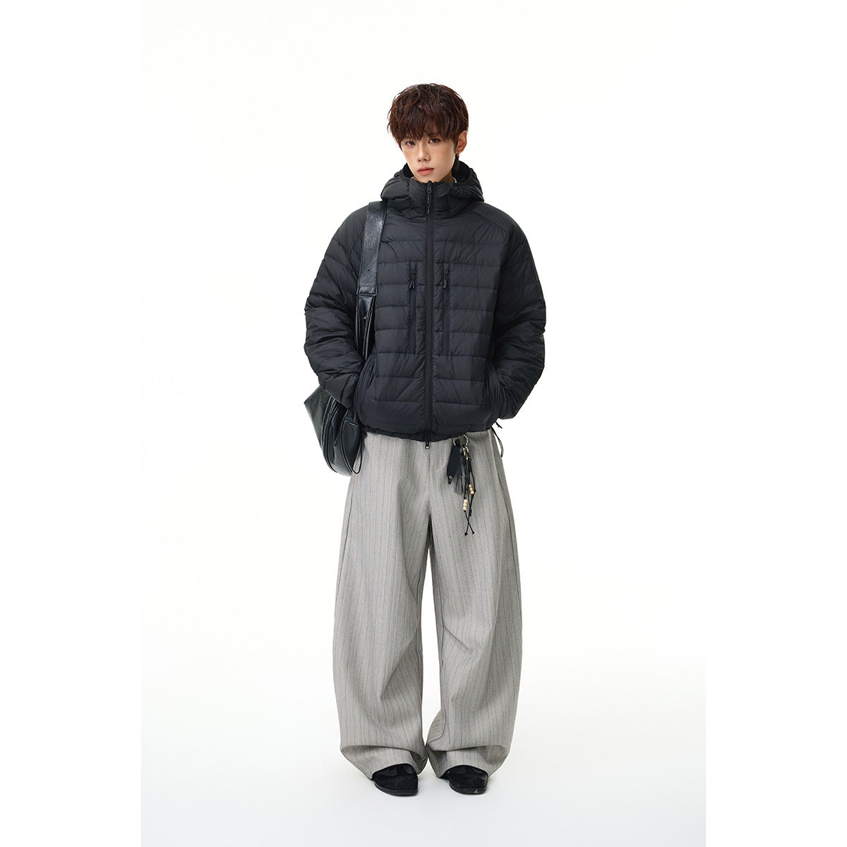 Full-length model wearing a black hooded puffer jacket with horizontal quilting, zip pockets, and light gray wide-leg