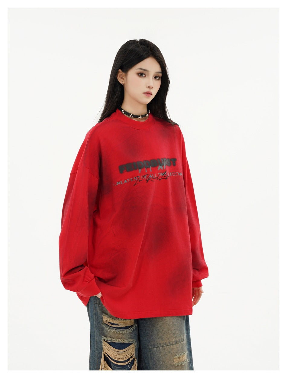 Model wearing an oversized red long-sleeve top with dark spots and chest print, styled with distressed jeans, side angle
