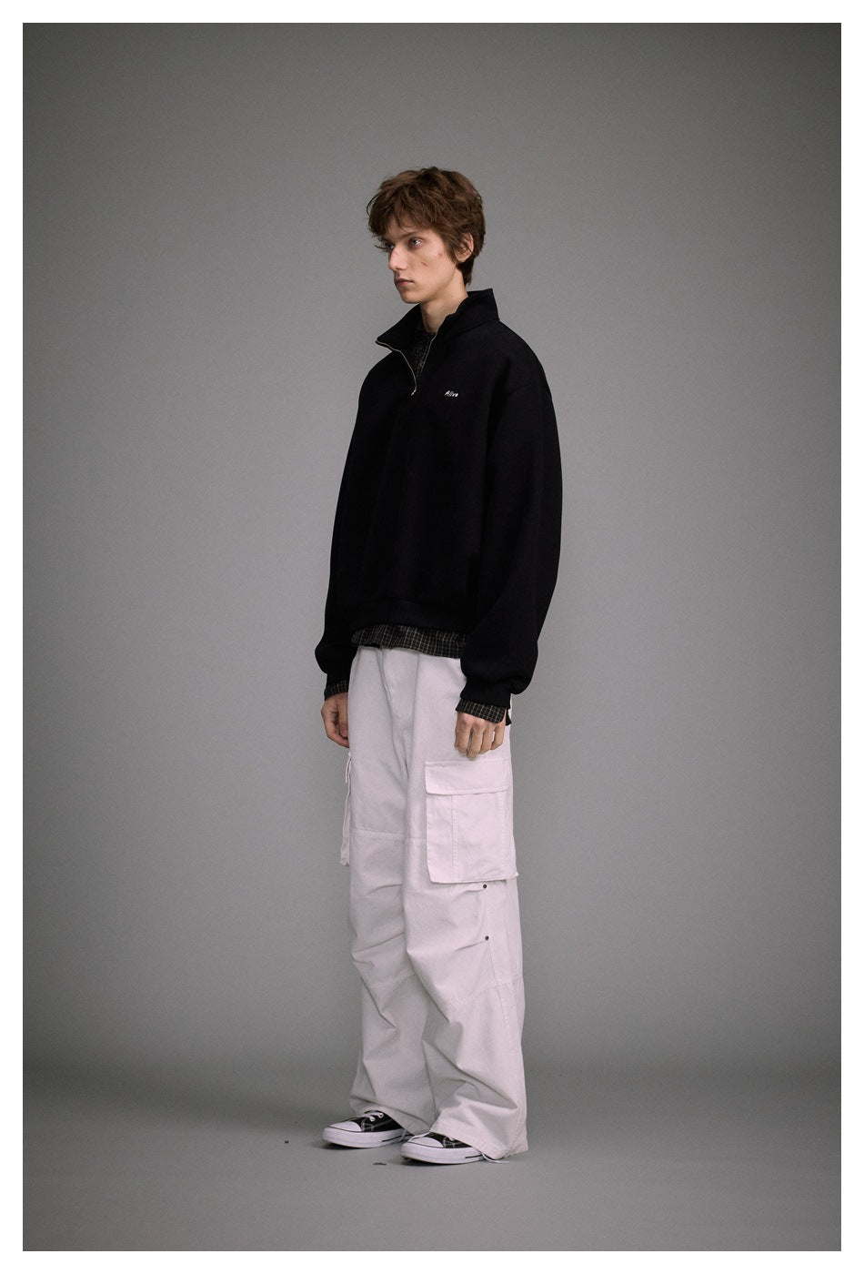 Model in black quarter-zip sweatshirt with white cargo pants, side view