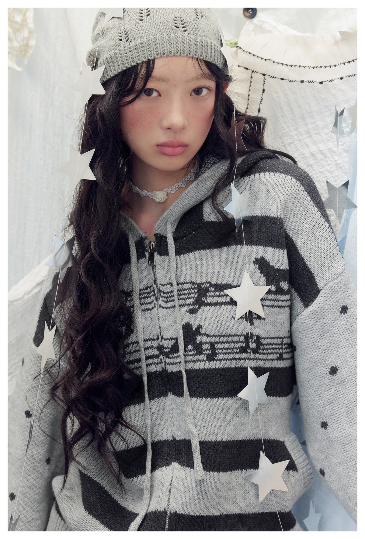 Close view of a model wearing a gray and black hooded zip-up sweater with animal motifs and dotted sleeves.
