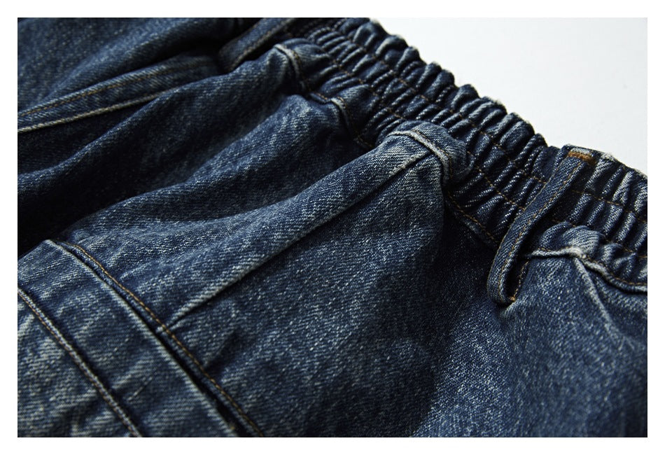 Close-up of blue denim shorts showing the gathered waistband, belt loop and pocket stitching.