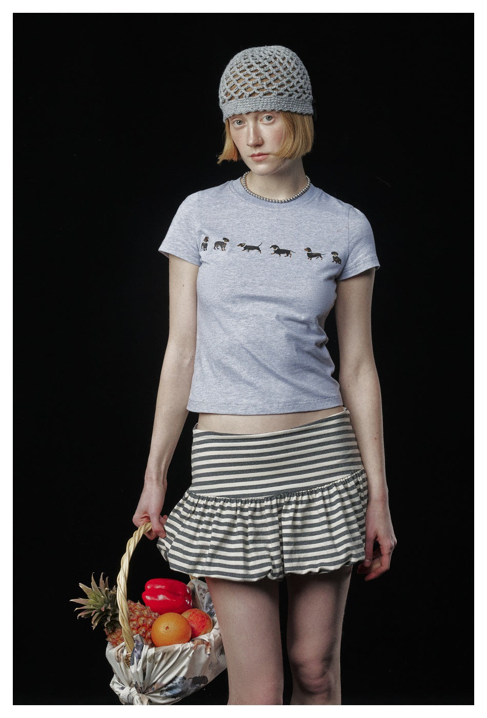 Model in a pale gray dog-print T-shirt and gray-and-white striped ruffle skirt, with an open-knit gray beanie.