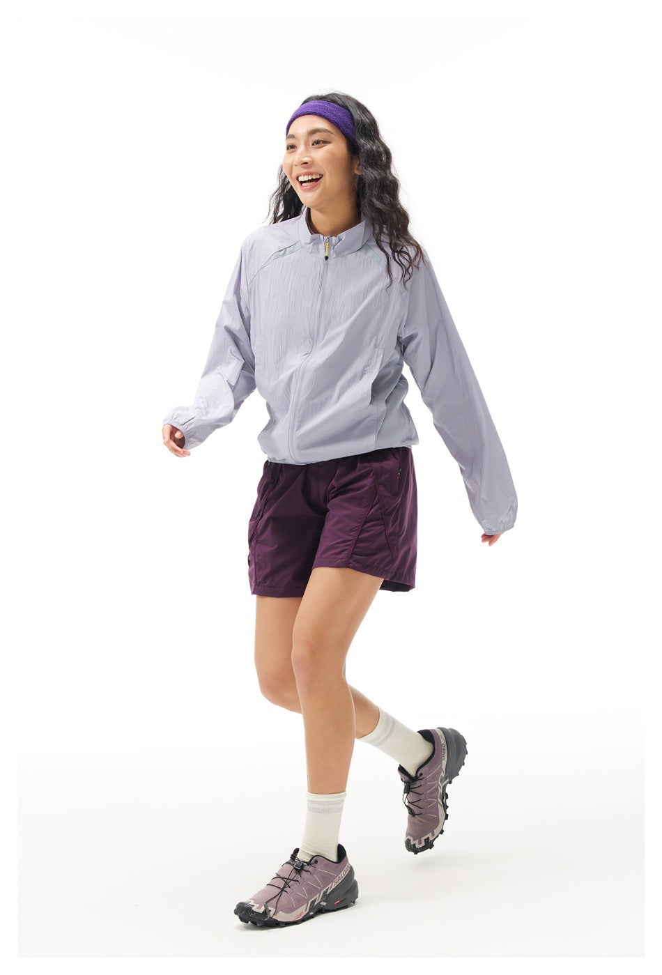 Model in a light lavender zip-up jacket and plum shorts, shown mid-step from a three-quarter angle.