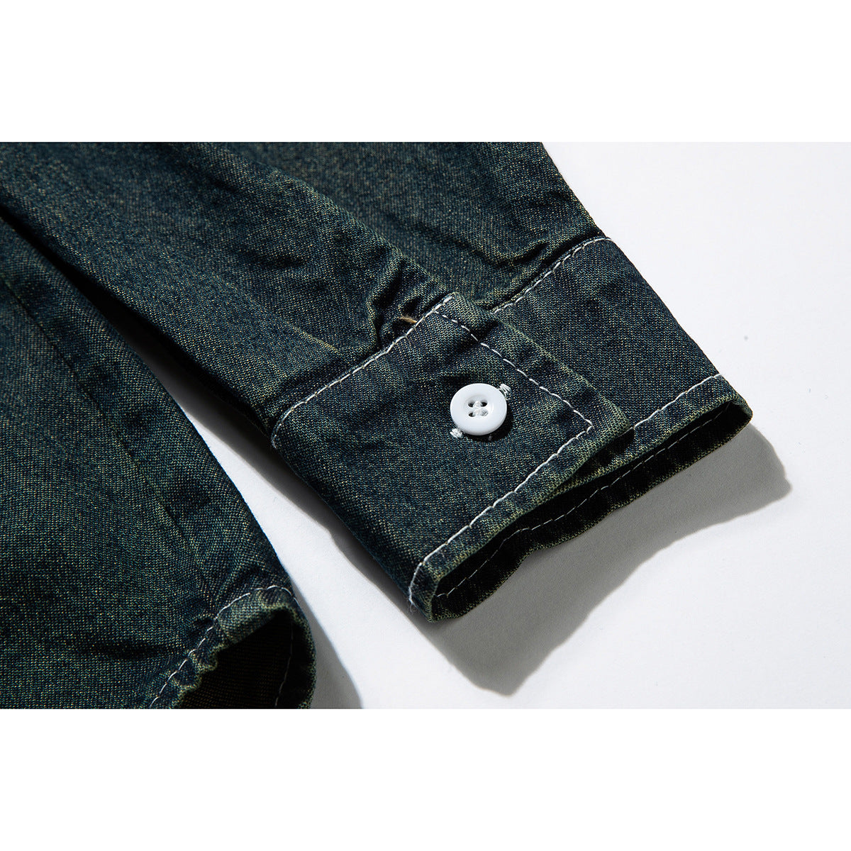 Close-up of the dark blue-green shirt sleeve cuff, showing a white button and contrasting stitching.