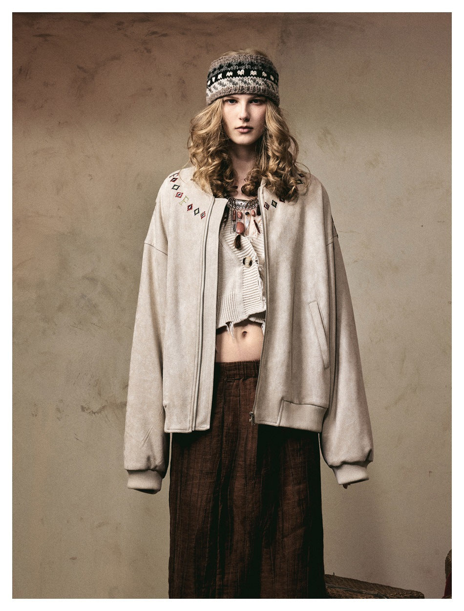 Front view of a model wearing an oversized cream zip jacket with embroidered shoulder motifs and ribbed cuffs.
