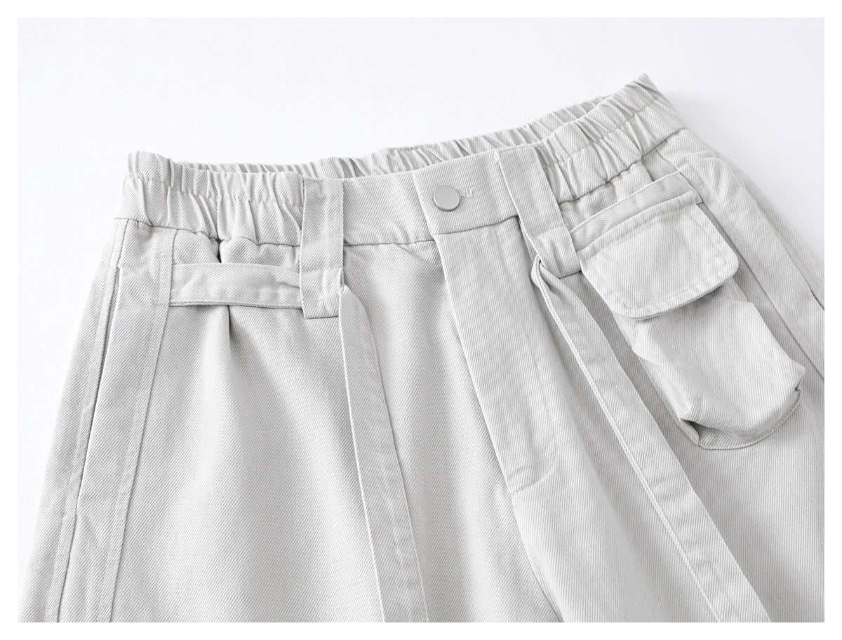Close-up of light gray trousers showing an elastic waist, button, belt loops and a flap utility pocket.
