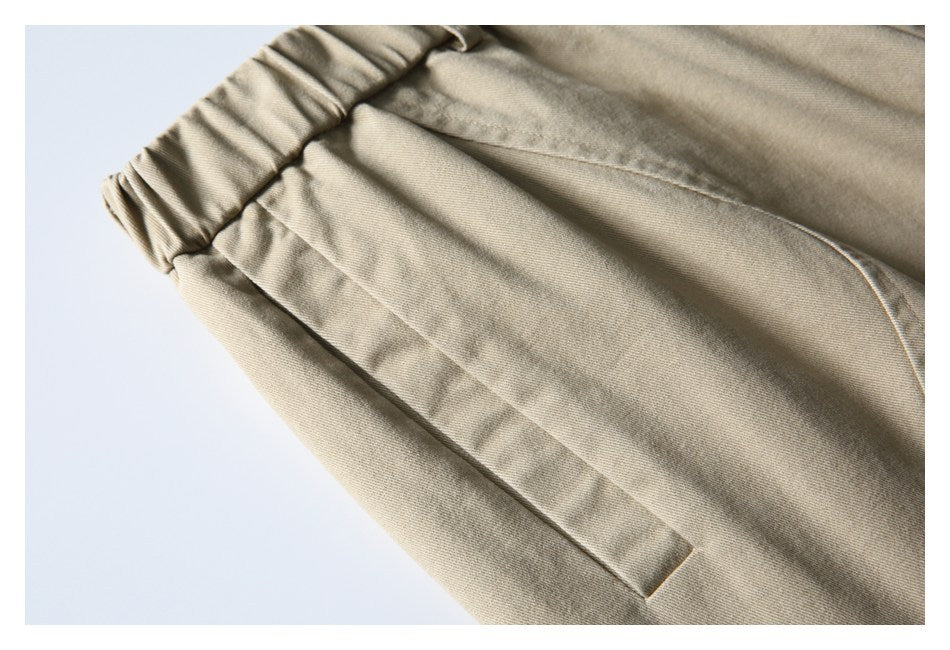 Close-up of beige shorts showing the gathered elastic waistband and a slanted front pocket.