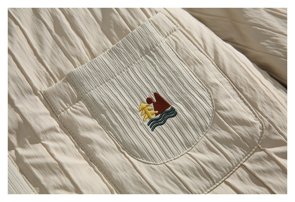 Close-up of a rounded chest pocket with a colorful embroidered graphic on the ivory quilted jacket.