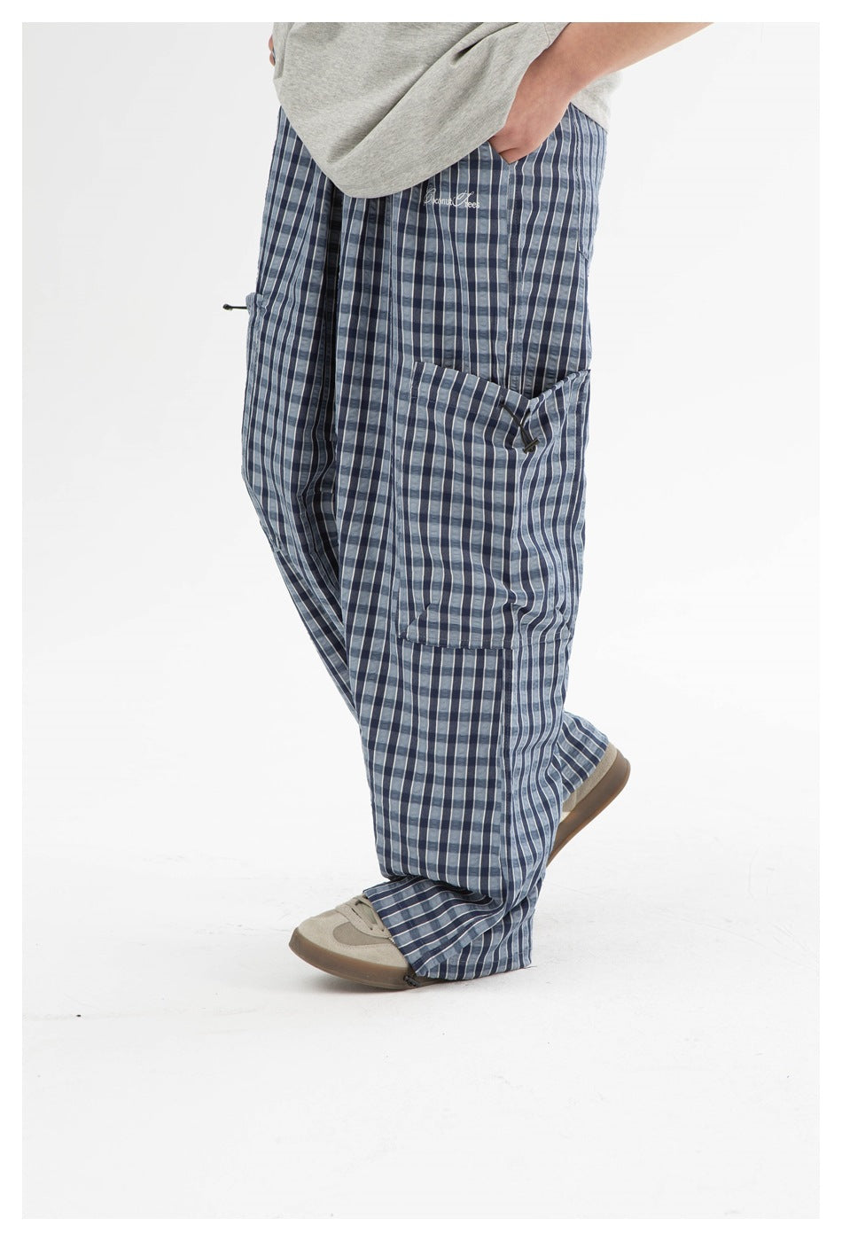 Side view of a model wearing blue plaid cargo pants, showing the large flap pocket and embroidered script.