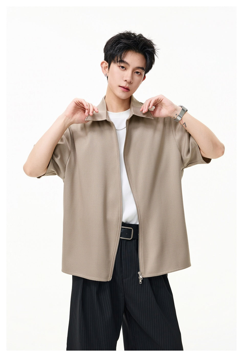 Model wearing an unzipped tan short-sleeve collared shirt over a white tee with black pinstripe pants
